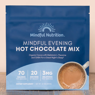 A pouch of Mindful Nutrition's Mindful Evening Hot Chocolate Mix with an image of a cup of hot chocolate with a spoon in it, on a wooden surface.