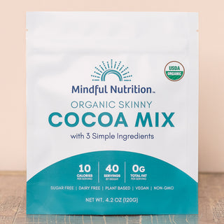 A pouch of Mindful Nutrition Organic Skinny Cocoa Mix with 3 Simple Ingredients. The packaging is white with a blue sun graphic and text detailing the product as sugar-free, dairy-free, plant-based, vegan, and non-GMO.