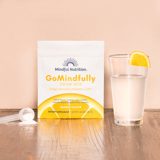 A resealable pouch of GoMindfully Orange drink mix by Mindful Nutrition, with a glass and a scoop.